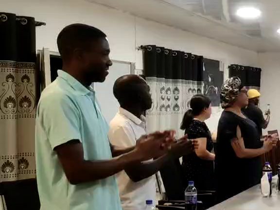 Tanzanian and Chinese colleagues standing round the table, clapping and singing