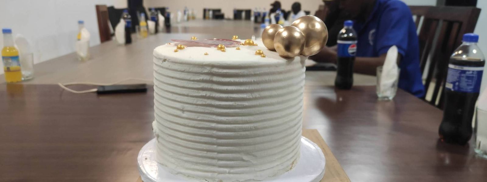 A white birthday cake decorated with gold pearls on the meeting-room table