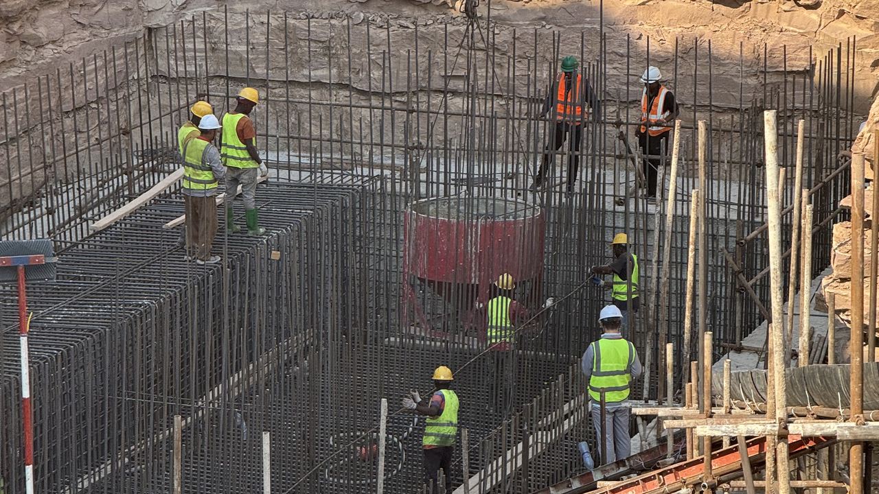 A red concrete skip being lowered by crane into the reinforced sump pit, with workers guiding it