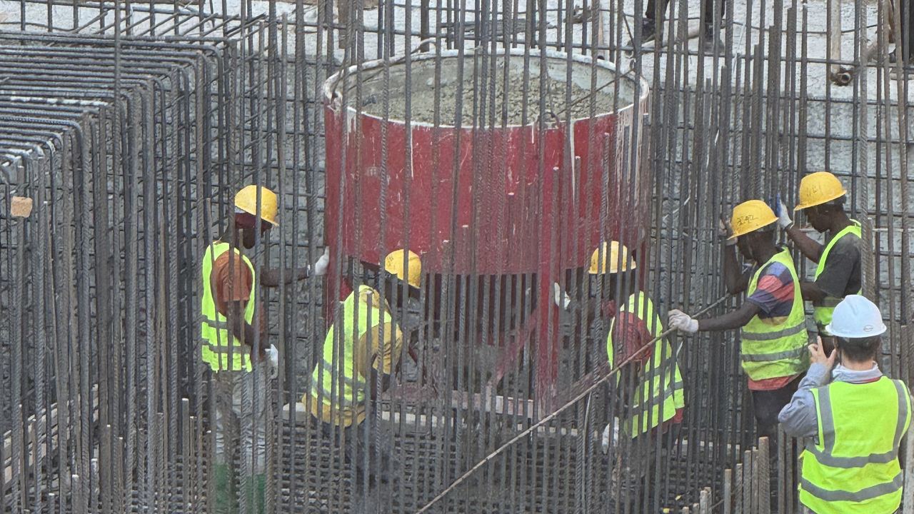 Red concrete skip being lowered into the reinforced sump pit while workers guide it