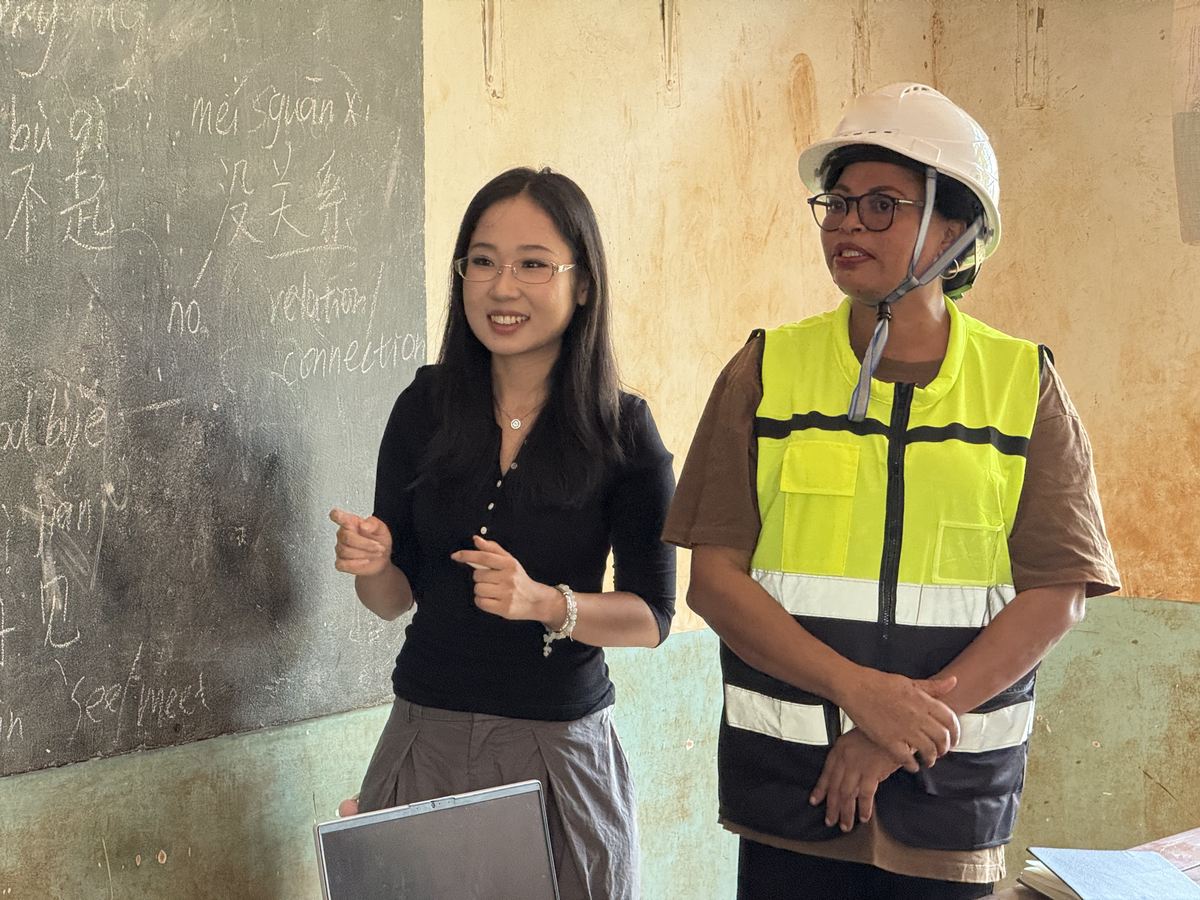 Volunteer teacher Ms Lan at the blackboard beside her teaching assistant in a hard hat and safety vest
